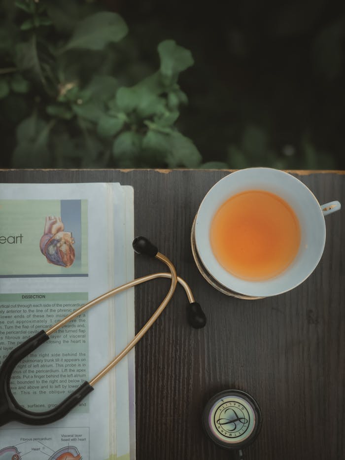 Flat lay of tea cup, stethoscope, and heart health book on wooden surface.